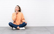 © luismolinero - Young woman with curly hair sitting on the floor thinking an idea