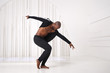 Elegant black man dancer in black clothes is dancing in a bright room.