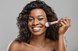 Attractive black girl using brush tool, applying blush on face