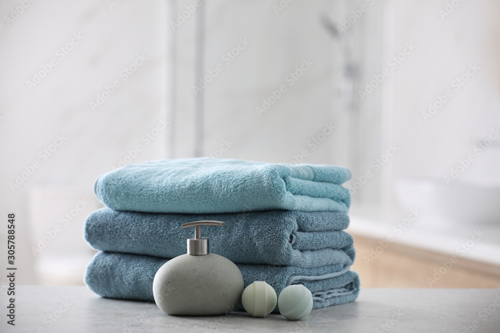Stack of fresh towels, soap dispenser and bath bombs on table indoors - obrazy, fototapety, plakaty 