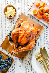 Roasted whole turkey on a festive table with persimmon, blue grape and lemon for family Thanksgiving Holiday. Top view, flat lay.