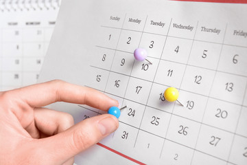 Woman marking date in calendar with drawing pin, closeup