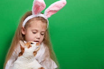 cute happy chikd girl with a real easter pet cat wearing ears on green background