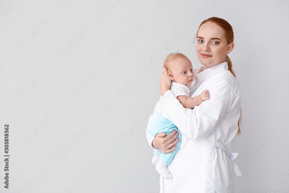 Pediatrician with cute baby on light background