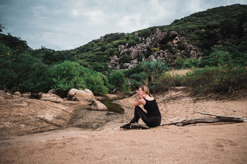 Wall Mural - Young sporty skinny girl sitting on the beach and relaxing, sand and fresh green grass around