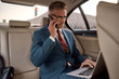 © Svitlana - Discussing project details. Confident and stylish mature businessman in full suit working on his laptop and talking on the phone with business partner while sitting in the car