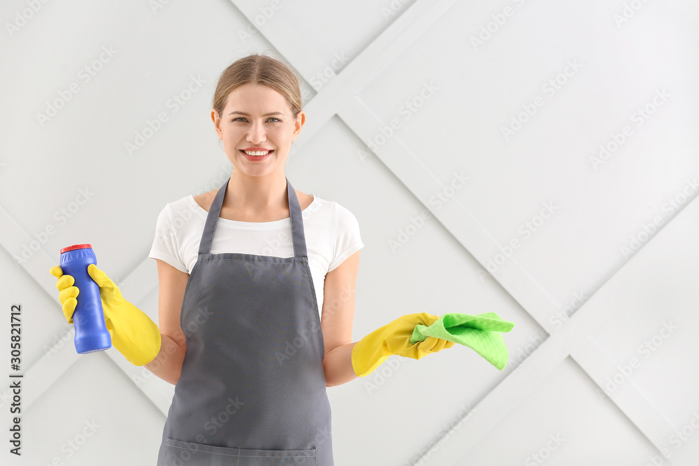 Female janitor with cleaning supplies on grey background