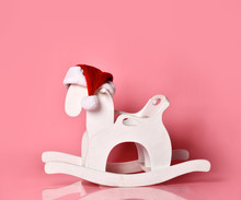Christmas Antique Rocking White Horse Toddler Toy In New Year Red Hat On Pink 