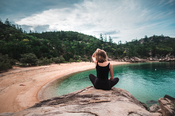 Wall Mural - Young girl enjoying view from the top of the rock over the bay with turquoise water and sandy beach