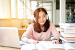 © sahachat - Young woman in a good mood listening to music  while studying in a library