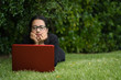 © Pajaros Volando - young woman lying down on the grass of a park while watching the screen of her laptop. Natural Environment. Technological concept