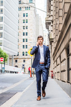Modern Daily Life. Young Handsome Man Traveling In New York City, Wearing Blue Suit, White Shirt, Brown Leather Shoes, Hand In Pocket, Walking On Street With High Buildings, Talking On Cell Phone..
