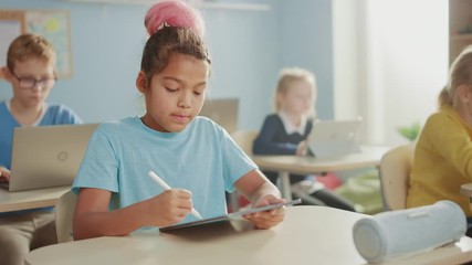 Wall Mural - Elementary School Computer Science Class: Cute Girl Uses Digital Tablet Computer, Her Classmates work with Laptops too. Children Getting Modern Education in STEM, Playing and Learning