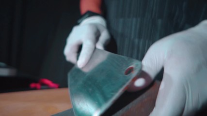 Hands of cook wearing white gloves sharpen big kitchen knife with a sharpening stone over chopping board