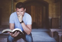 Closeup Shot Of A Male Sitting While Reading The Bible With A Blurred Background