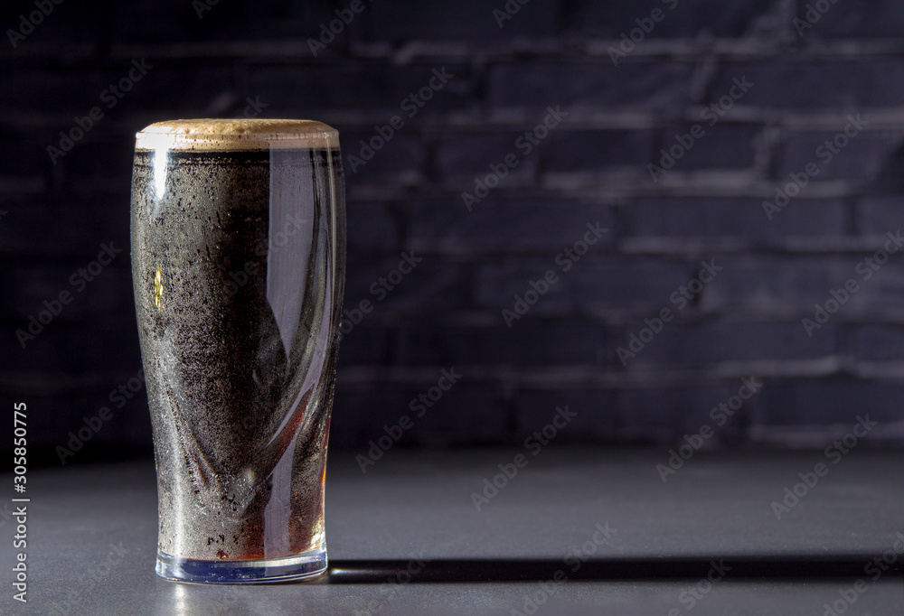 A dark Irish dry stout beer glass with a black brick on the background - obrazy, fototapety, plakaty 