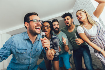 Happy friends singing together at home. Karaoke party concept