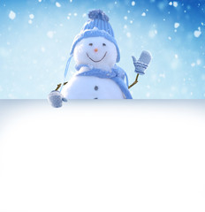 Merry Christmas and happy New Year greeting card.   Snowman standing in winter Christmas landscape and points to a white billboard.