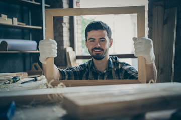 Wall Mural - Photo of cheerful cute man having finished making frame holding it looking through wooden handmade smiling toothily at you