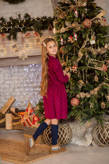 Wall Mural -  A girl near the Christmas tree. Beautiful child decorates a Christmas tree. Portrait of a girl with long hair