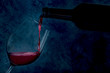 Wine poured into a glass from a bottle, on a dark background with copy space, toned image