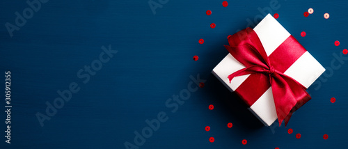 Fotomural White gift box with red ribbon bow on blue background with confetti