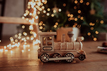 Handmade Wooden Train In Lots Of Yellow Garland, On A Dark Wooden Floor, Christmas Tree On The Background