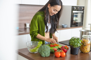 Smiling young woman slicing carrots and tomatoes