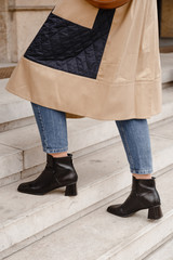 street style portrait of an attractive woman wearing a beige trench coat, denim jeans and black ankle boots, crossing the street. fashion outfit perfect for autumn fall winter