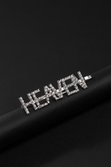 Subject shot of a silver hair clip made as a sign plate with sparkling crystal lettering 