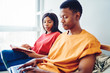 © BullRun - Serious african american woman looking at her boyfriend typing on laptop computer searching website for making online booking in bed room, dark skinned couple shopping in web store via netbook.