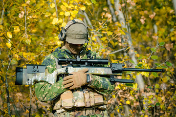 Wall Mural - Airsoft man in uniform hold sniper rifle on yellow forest backdrop. Side view