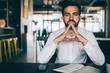 © BullRun - Portrait of serious Caucasian male entrepreneur in white shirt looking at camera while thinking on information, formally dressed man pondering on productive strategy sitting at cafeteria table indoors