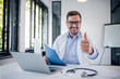 © bnenin - Portrait of a smiling doctor showing thumbs-up.