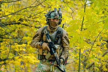 Wall Mural - Airsoft man in uniform with machine gun standing on yellow forest backdrop. Horizontal photo