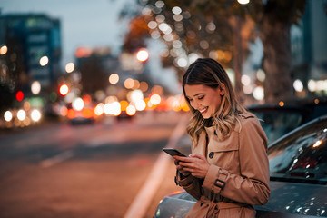 City, technology and people. Cute cheerful girl using phone in the city street.