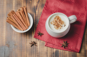 Eggnog. Traditional christmas cocktail in a white mug with cinnamon sticks  and anise on a red napkin. Top view. Wooden background.