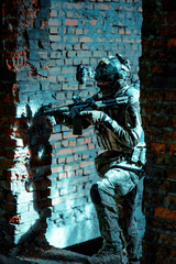 Wall Mural - Man in uniform with machine gun and night-vision device move between two broken walls. Airsoft soldier in night building. Vertcal photo