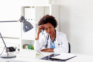 Woman doctor on stress sitting at desk with hand on head in ambulance