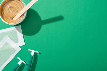 Wall Mural - top view of green disposable razors, wax and depilation stripes on green background