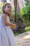 Fototapeta  - A girl in the garden and white dress, with natural yellow flowers in her hand and very attentive look