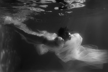 Beautiful girl swims underwater with long hair. Blue or gold background like gold. The atmosphere of a fairy tale or magic. Diving under the water with a shiny cloth