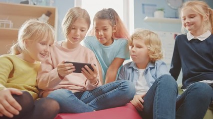 Fototapete - Kids Browsing on Internet and Playing Online Video Games on Mobile Phone, Watching Videos. Diverse Group of Cute Small Children Sitting together on the Bean Bags Use Smartphone and Talk, Have Fun