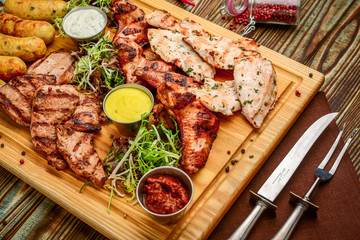 Assorted delicious grilled meat and vegetables with fresh salad and bbq sauce on cutting board on wooden background. Big set of Hot Meat Dishes