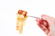 © teine - Reginette pasta with bolognese sauce decorated with parmesan on a fork on a white background, held by a female hand