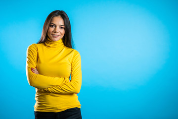 Copy space. Beautiful cheerful mixed race woman in yellow clothing smiling to camera over blue wall background. Cute hispanic girl's portrait.