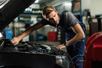 Wall Mural - Young mechanic recharging air conditioner unit of a car in repair workshop.