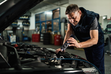 Wall Mural - Auto mechanic using lap while examining car engine in repair shop.