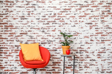 Cozy armchair with table and plant near brick wall in room