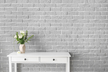 Fresh flowers in vase on table near brick wall